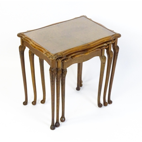 1599 - A mid / late 20thC nest of three burr walnut topped tables raised on acanthus carved legs terminatin... 