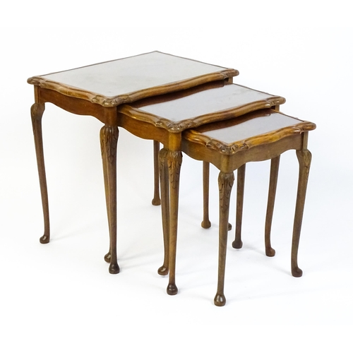 1599 - A mid / late 20thC nest of three burr walnut topped tables raised on acanthus carved legs terminatin... 