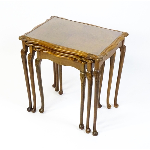 1599 - A mid / late 20thC nest of three burr walnut topped tables raised on acanthus carved legs terminatin... 