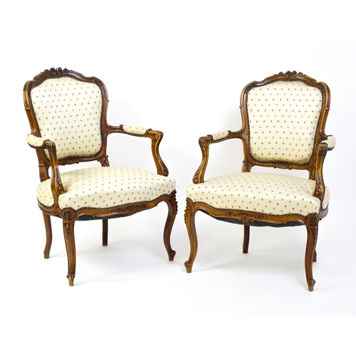 1607 - A pair of Louis XV style fauteuil open armchairs with floral carved cresting rails, swept arms,  uph... 