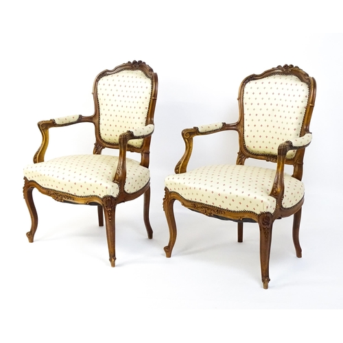 1607 - A pair of Louis XV style fauteuil open armchairs with floral carved cresting rails, swept arms,  uph... 