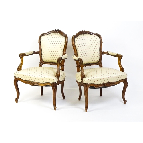 1607 - A pair of Louis XV style fauteuil open armchairs with floral carved cresting rails, swept arms,  uph... 