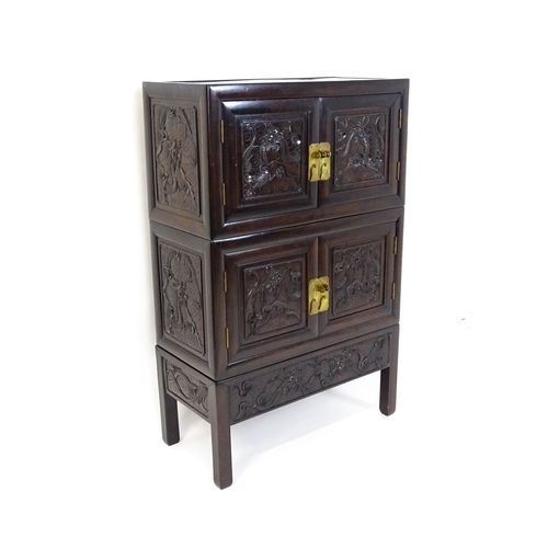 1614 - An oriental rosewood cabinet of three tiers, the top two sections having panelled carved doors depic... 