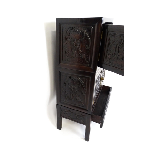 1614 - An oriental rosewood cabinet of three tiers, the top two sections having panelled carved doors depic... 