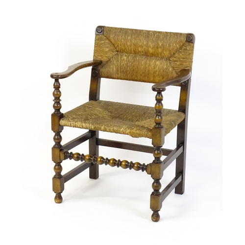 1622 - An early 20thC Wylie & Lochhead elbow chair with a rush back and envelope rush seat, carved roundels... 