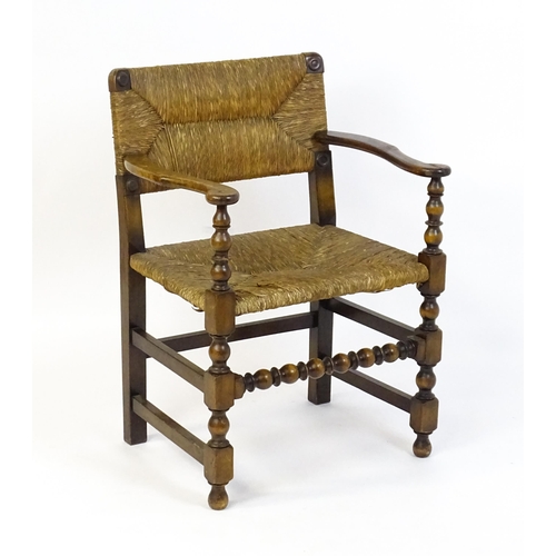 1622 - An early 20thC Wylie & Lochhead elbow chair with a rush back and envelope rush seat, carved roundels... 