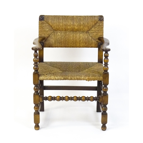 1622 - An early 20thC Wylie & Lochhead elbow chair with a rush back and envelope rush seat, carved roundels... 