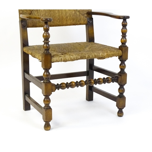 1622 - An early 20thC Wylie & Lochhead elbow chair with a rush back and envelope rush seat, carved roundels... 