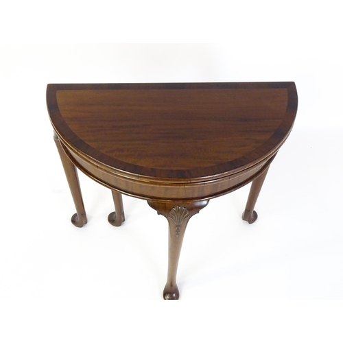 1660 - A 20thC mahogany demi lune card table with a hinged top opening to show a baize playing surface rais... 