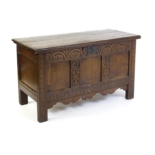 1672 - An early 18thC oak coffer of peg jointed construction, with a hinged lid and a carved, panelled fron... 