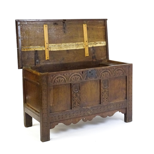 1672 - An early 18thC oak coffer of peg jointed construction, with a hinged lid and a carved, panelled fron... 