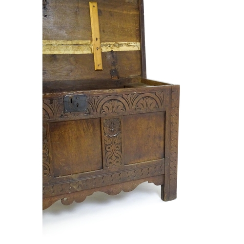 1672 - An early 18thC oak coffer of peg jointed construction, with a hinged lid and a carved, panelled fron... 