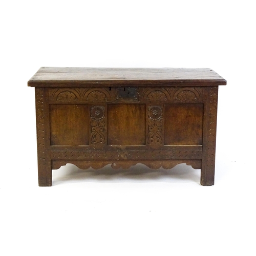 1672 - An early 18thC oak coffer of peg jointed construction, with a hinged lid and a carved, panelled fron... 