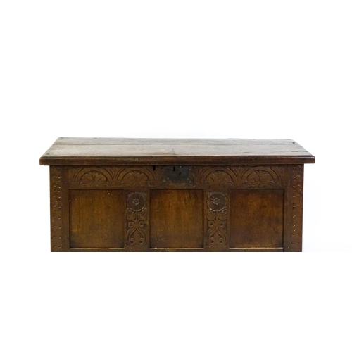 1672 - An early 18thC oak coffer of peg jointed construction, with a hinged lid and a carved, panelled fron... 