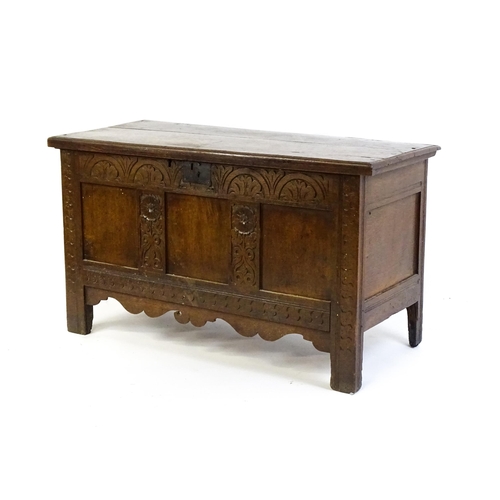 1672 - An early 18thC oak coffer of peg jointed construction, with a hinged lid and a carved, panelled fron... 