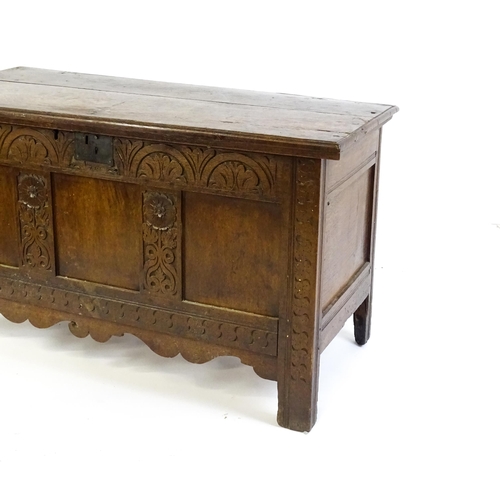 1672 - An early 18thC oak coffer of peg jointed construction, with a hinged lid and a carved, panelled fron... 