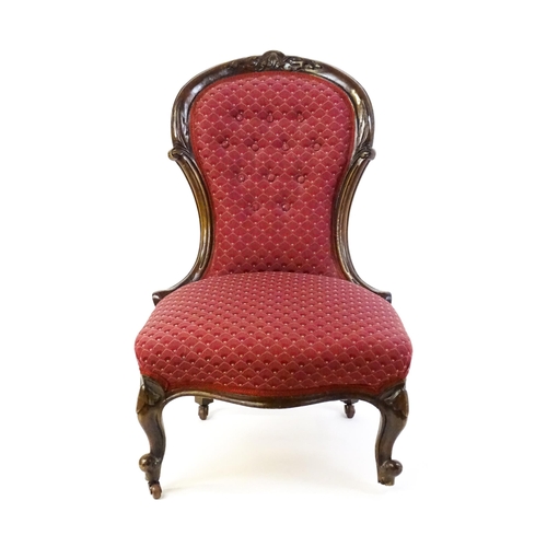 1696 - A late 19thC / early 20thC nursing chair with a deep buttoned spoon back adorned with a carved crest... 