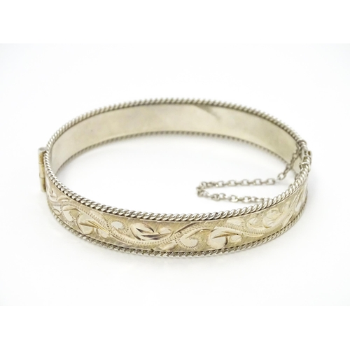 785 - A silver bracelet of bangle form with engraved foliate decoration. Approx. 2 1/2