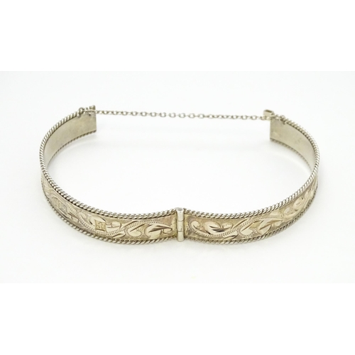 785 - A silver bracelet of bangle form with engraved foliate decoration. Approx. 2 1/2