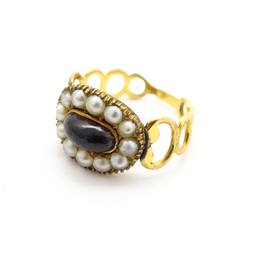 809 - Memorial / Mourning Jewellery: A 19thC gold ring set with central garnet cabochon bordered by seed p... 