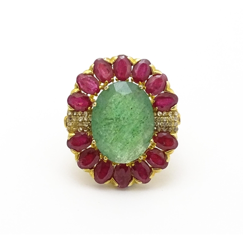 830 - A gilt metal dress ring set with central emerald coloured stone bordered by ruby coloured stones fla... 