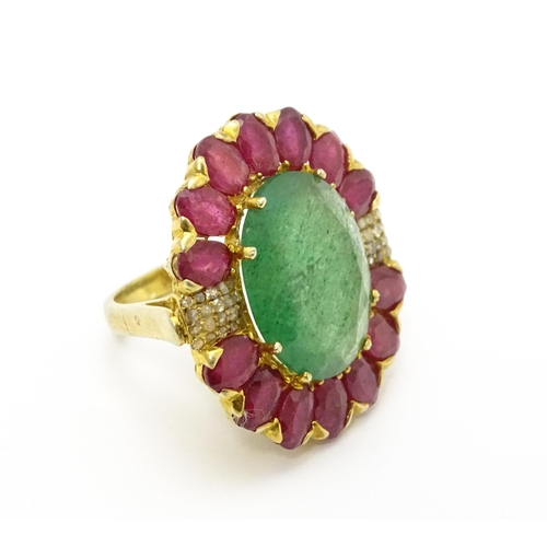 830 - A gilt metal dress ring set with central emerald coloured stone bordered by ruby coloured stones fla... 