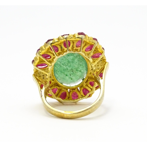 830 - A gilt metal dress ring set with central emerald coloured stone bordered by ruby coloured stones fla... 