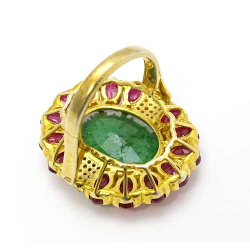 830 - A gilt metal dress ring set with central emerald coloured stone bordered by ruby coloured stones fla... 