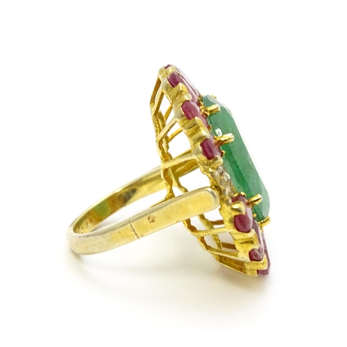 830 - A gilt metal dress ring set with central emerald coloured stone bordered by ruby coloured stones fla... 