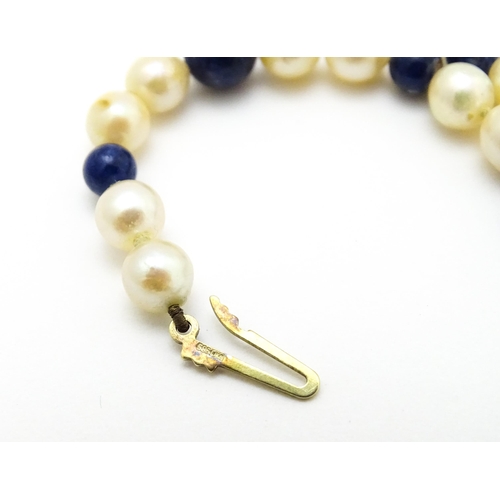 898 - A pearl and lapis lazuli necklace, the 14ct gold clasp set with diamonds and red stones. Approx. 36