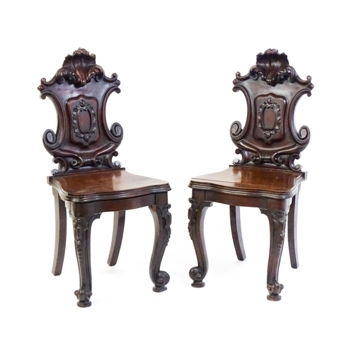 1545 - A pair of Victorian mahogany hall chairs with heavily carved tops above waisted backrests with armor... 