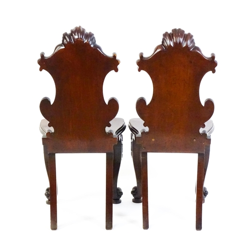 1545 - A pair of Victorian mahogany hall chairs with heavily carved tops above waisted backrests with armor... 