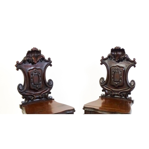 1545 - A pair of Victorian mahogany hall chairs with heavily carved tops above waisted backrests with armor... 