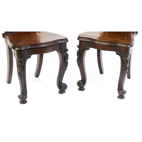 1545 - A pair of Victorian mahogany hall chairs with heavily carved tops above waisted backrests with armor... 