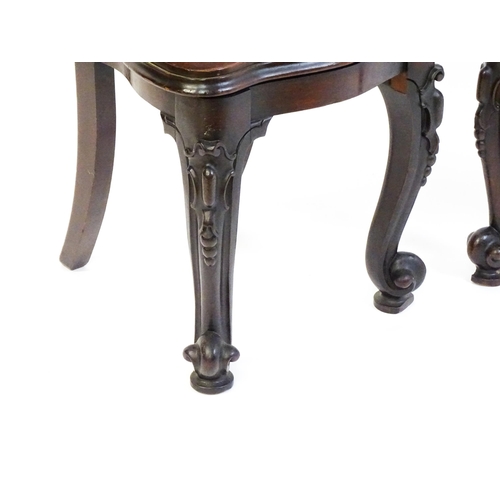 1545 - A pair of Victorian mahogany hall chairs with heavily carved tops above waisted backrests with armor... 