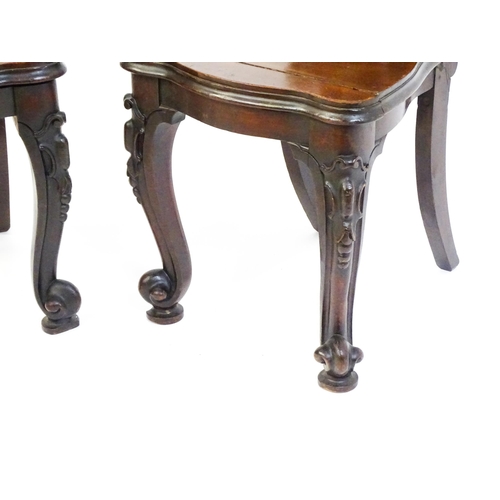 1545 - A pair of Victorian mahogany hall chairs with heavily carved tops above waisted backrests with armor... 