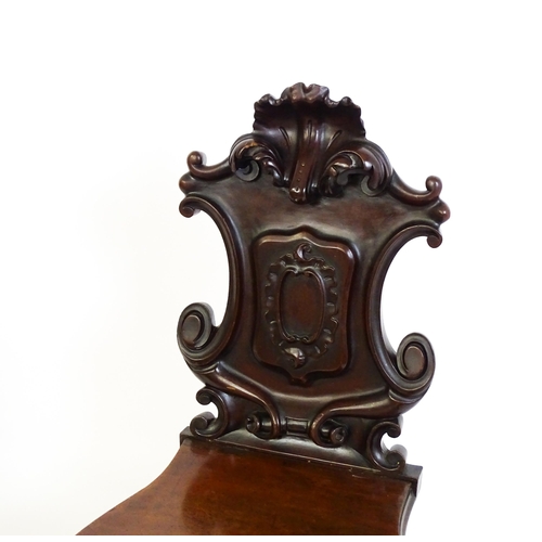 1545 - A pair of Victorian mahogany hall chairs with heavily carved tops above waisted backrests with armor... 