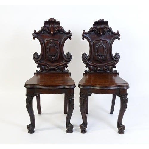 1545 - A pair of Victorian mahogany hall chairs with heavily carved tops above waisted backrests with armor... 