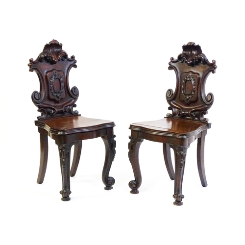 1545 - A pair of Victorian mahogany hall chairs with heavily carved tops above waisted backrests with armor... 