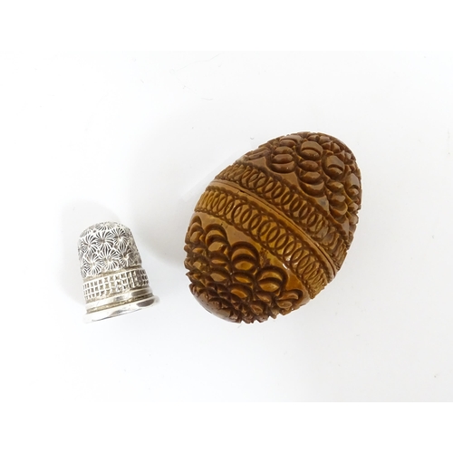 1153 - A 19thC carved coquilla nut of egg form with silver sewing thimble within, hallmarked Chester 1900, ... 