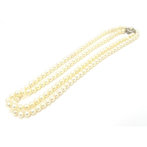 883 - A two-strand pearl necklace with 14ct (585) white gold clasp of floral form set with central pearl. ... 