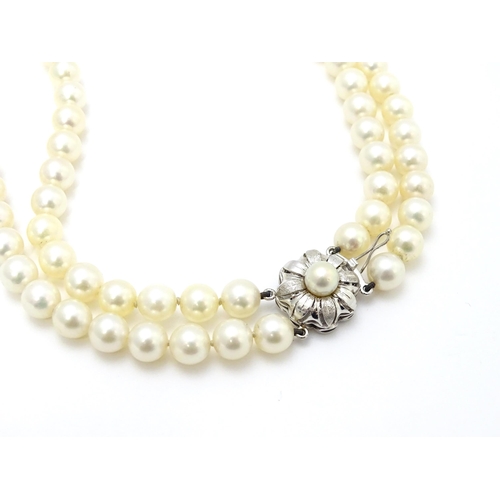 883 - A two-strand pearl necklace with 14ct (585) white gold clasp of floral form set with central pearl. ... 