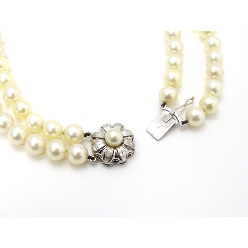 883 - A two-strand pearl necklace with 14ct (585) white gold clasp of floral form set with central pearl. ... 