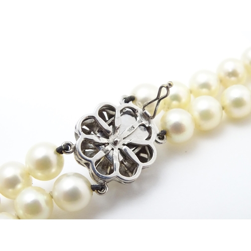 883 - A two-strand pearl necklace with 14ct (585) white gold clasp of floral form set with central pearl. ... 