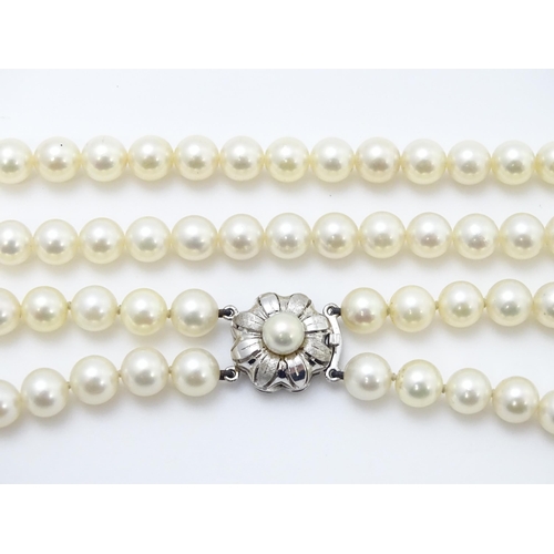 883 - A two-strand pearl necklace with 14ct (585) white gold clasp of floral form set with central pearl. ... 