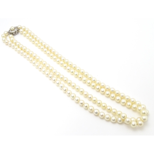 883 - A two-strand pearl necklace with 14ct (585) white gold clasp of floral form set with central pearl. ... 