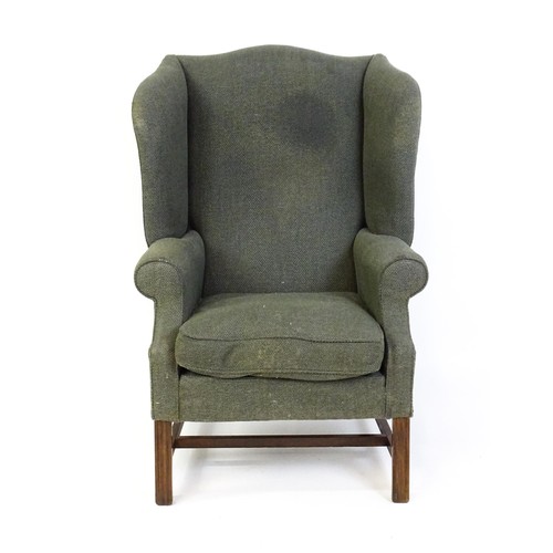 229 - An early 20thC wingback armchair raised on chamfered front legs united by a H stretcher. 33