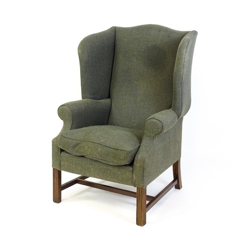 229 - An early 20thC wingback armchair raised on chamfered front legs united by a H stretcher. 33