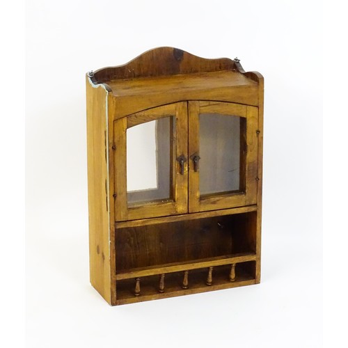 322 - A pine hanging wall cabinet, with two glazed doors above a small rack with a gallery of turned finia... 