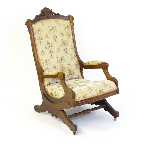 636 - An early 20thC rocking chair with carved cresting rail above a chamfered frame, with upholstered bac... 